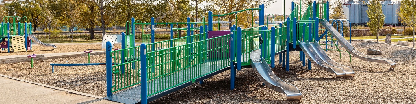 Accessible playground with ramps, slides, and green-and-blue play equipment in a park setting.