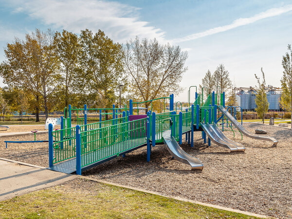 Accessible playground with ramps, slides, and green-and-blue play equipment in a park setting.