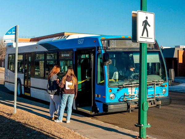 Two people standing at a bus stop, about to get on a bus.